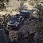 green Mazda Cx-50 SUV Towing Black Trailer Green Grass Trees Rocks