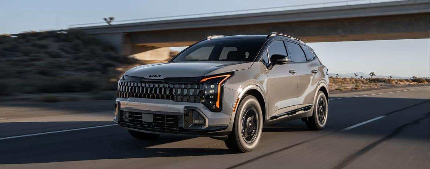 Tan 2026 Kia Sportage driving on a road with a bridge in the background.