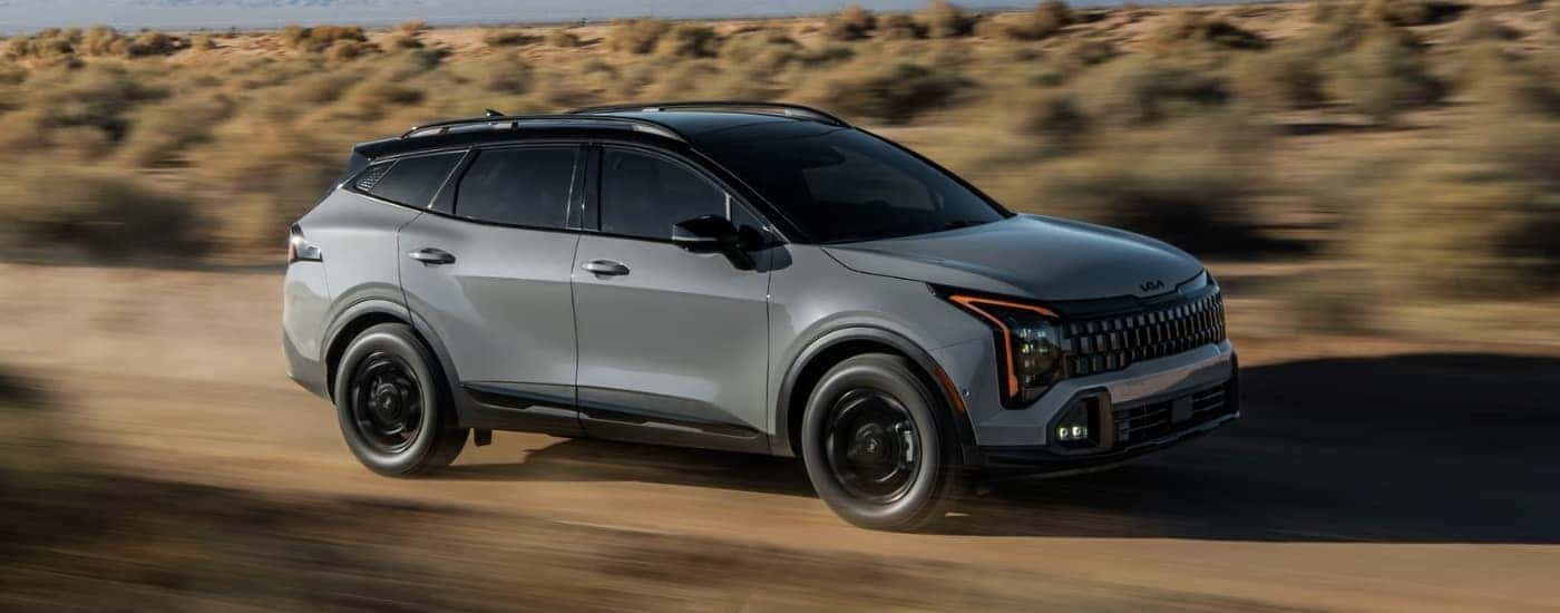 A gray 2026 Kia Sportage X-Pro Prestige driving a dirt road.