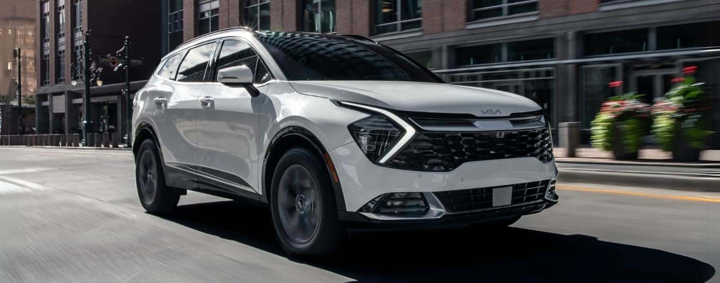 A white 2023 Kia Sportage Hybrid driving down a city street.