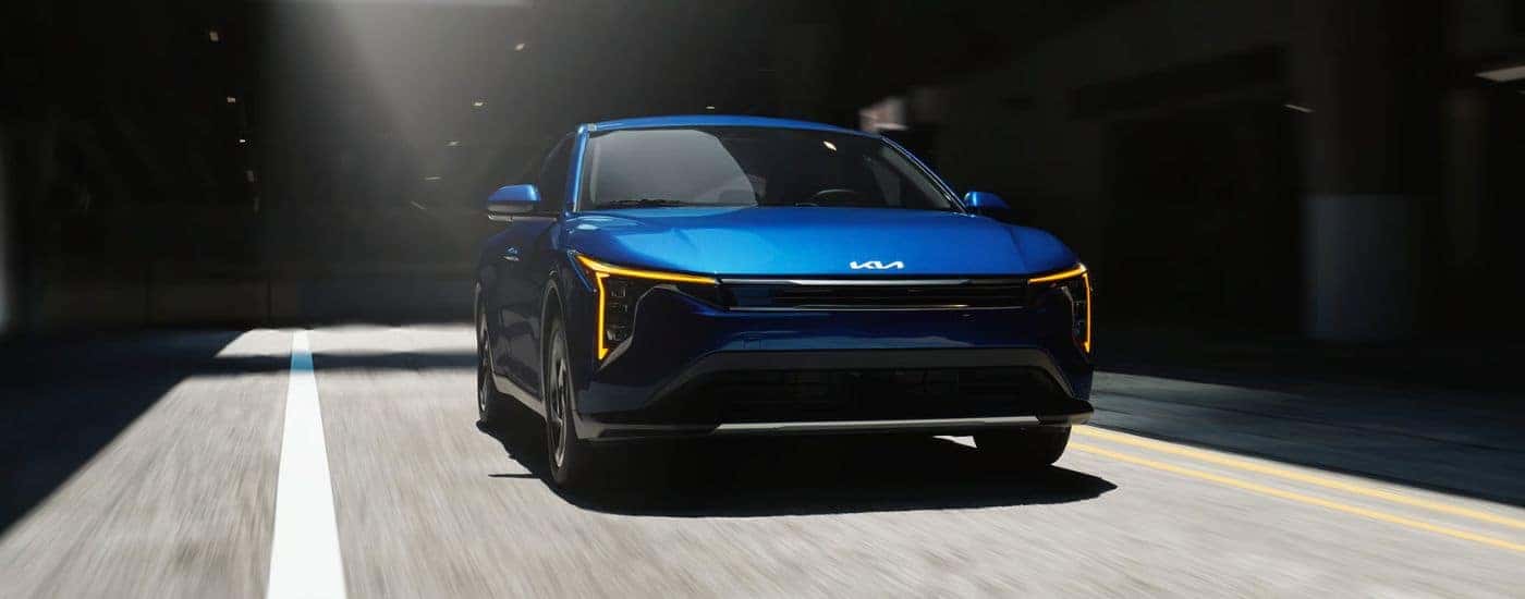 Head-on view of a blue 2026 Kia K4 EX shown driving out of a tunnel.