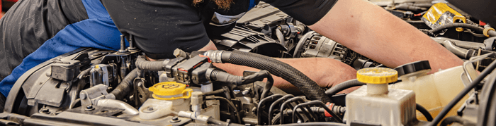 Image of service technician's arms working under the hood of a vehicle.