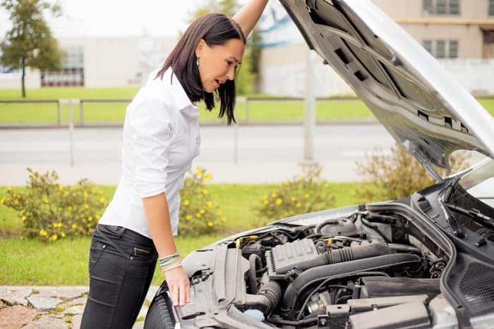 Woman looking under the hood of her broken car