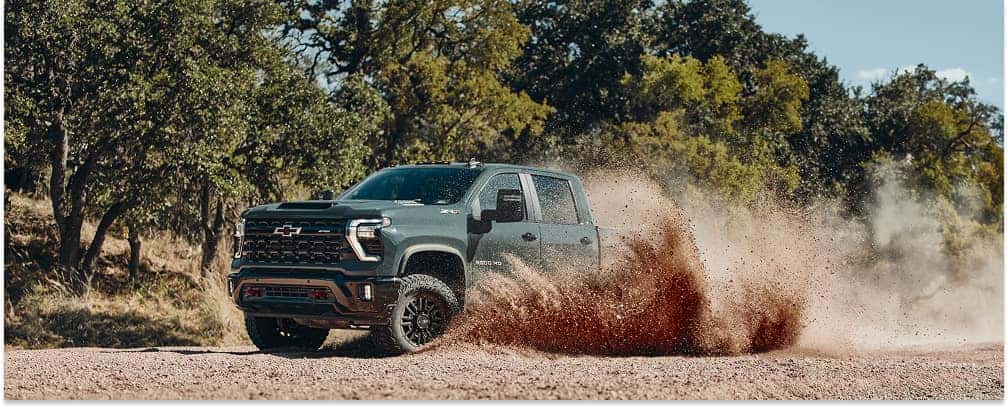 Front three-quarter view of a dark gray 2026 Chevrolet Silverado 2500 HD ZR2 kicking up dust on a dirt trail.