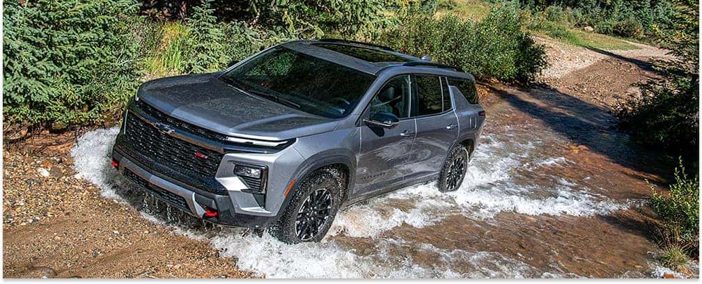 Front three-quarter view of a gray 2026 Chevrolet Traverse Z71 driving through a shallow water crossing.