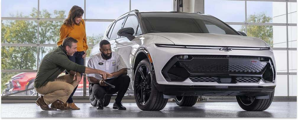 Chevrolet Certified Service technician discussing vehicle maintenance with customers next to a white Chevrolet SUV.