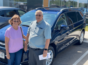Man and women in front of SUV with reciept of purchase smiling in front of car dealershipf 