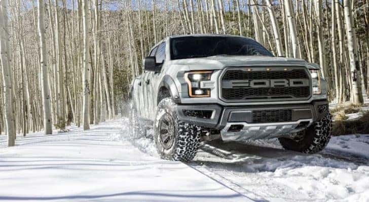 A silver 2017 Ford F-150 Raptor is shown driving through snow in the woods.