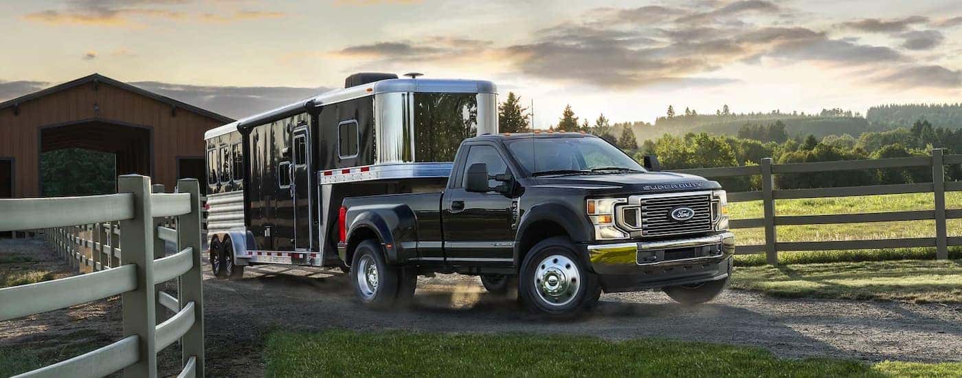 A black 2022 Ford F-450 Super Duty XL STX is shown towing a horse trailer past a fence.