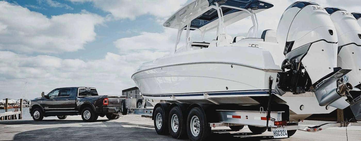 A black 2022 Ram 3500 is shown towing a large boat at a pier.