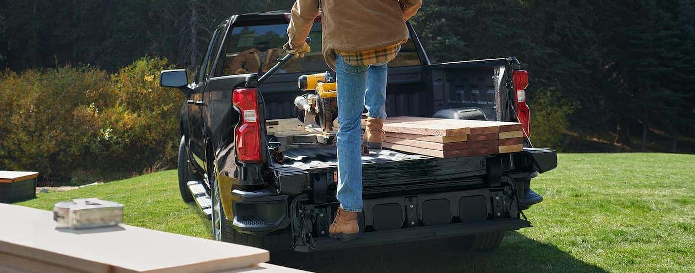A person is shown unloading lumber from the bed of a black 2022 Chevy Silverado 1500.