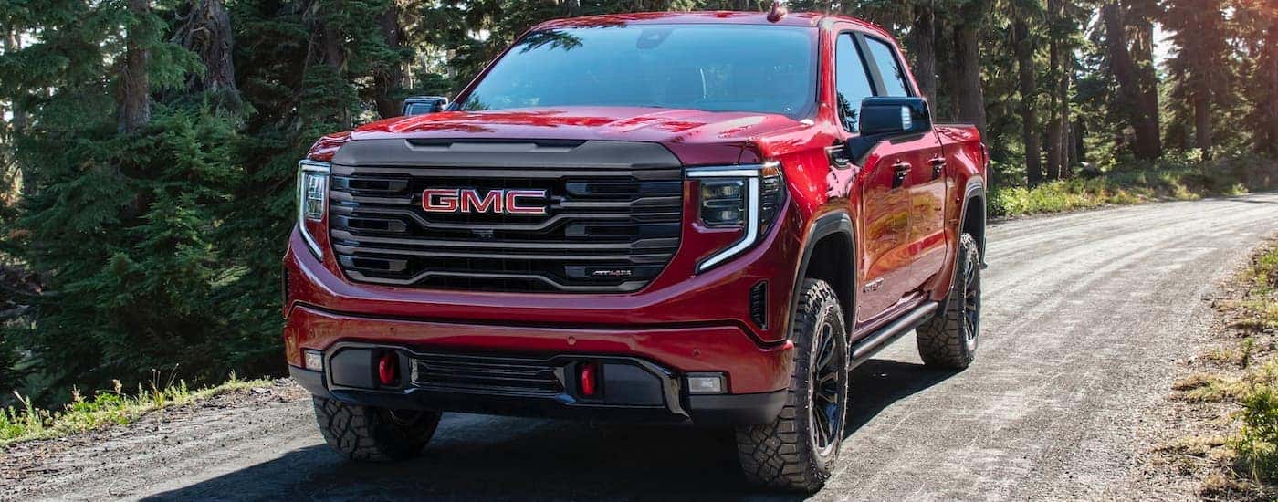 A red 2022 GMC 1500 Sierra AT4-X is shown driving down a woodland path.