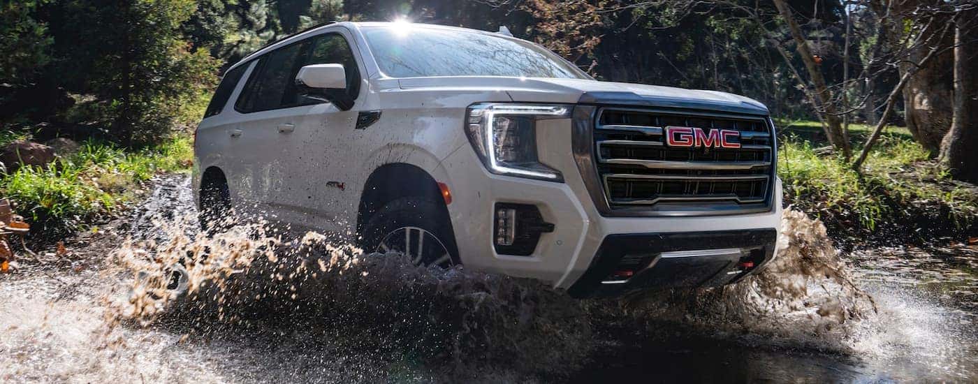 A white 2021 GMC Yukon AT4 is shown driving through a river during a 2022 GMC Yukon/Yukon XL and 2022 Chevy Tahoe/Suburban celebration.