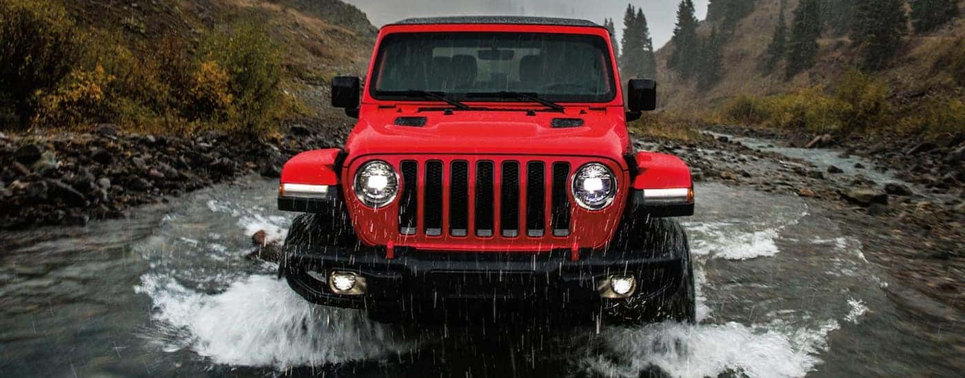 A red 2022 Jeep Wrangler Unlimited Rubicon is shown from the front driving through a river.