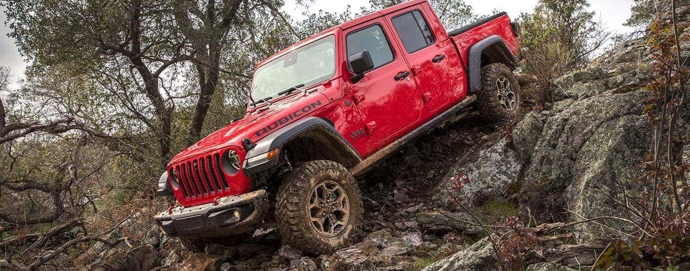 A red 2022 Jeep Gladiator Rubicon is shown off-roading on a steep muddy trail.