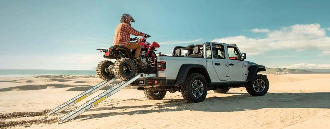 A person is shown driving an ATV into the bed of a white 2022 Jeep Gladiator Rubicon.