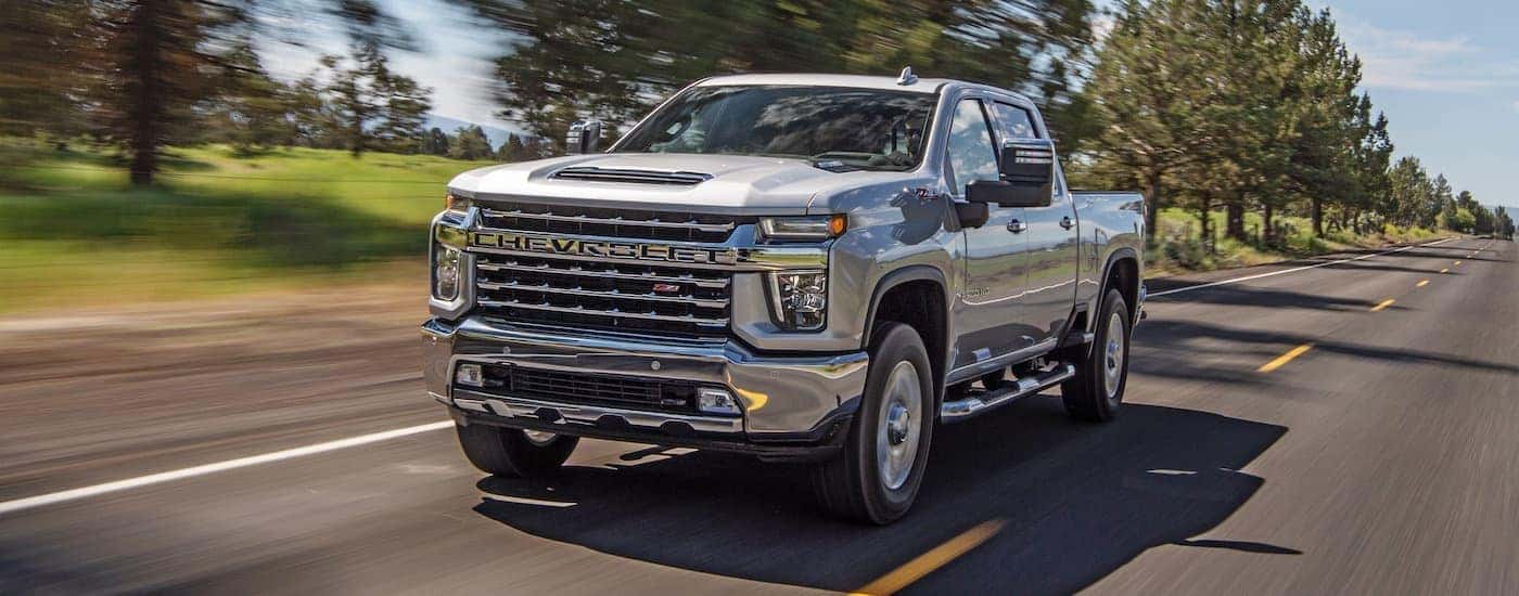 A silver 2022 Chevy Silverado 2500 HD Z71 is shown driving to a dealership to look at 2022 Chevy Silverado 2500/3500 vehicles in stock.