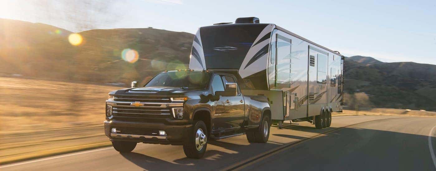 A black 2022 Chevy Silverado 3500 HD is shown towing a large trailer on a sunny day