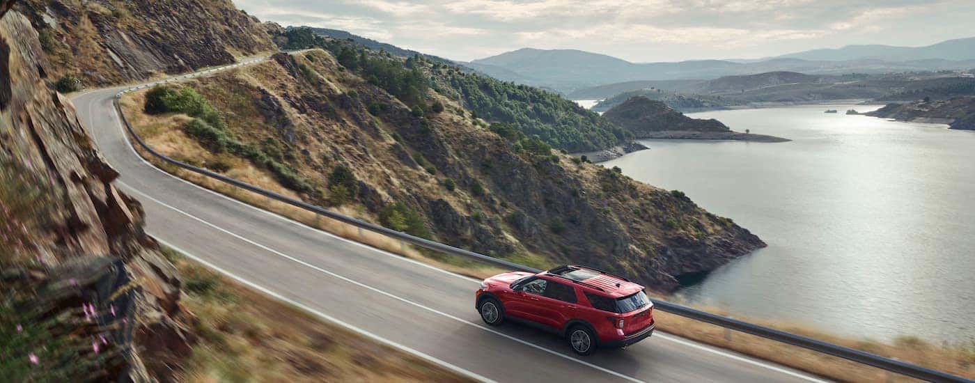 A red 2022 Explorer ST-Line is shown driving through a mountain road next to a lake.