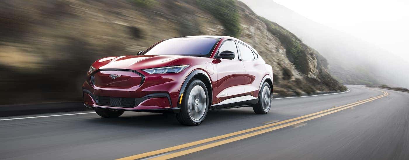 A red 2022 Ford Mustang Mach-E is shown driving past a rock face.