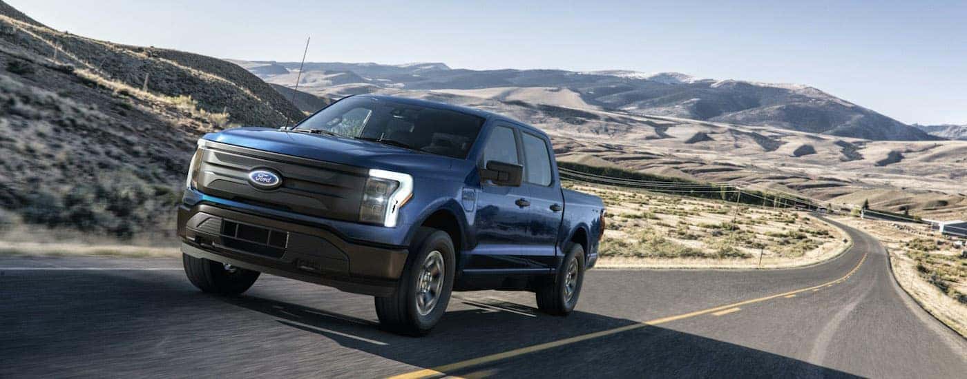 A dark blue 2022 Ford F-150 Lightning Pro is driving down an empty high way after visiting a Colorado Ford F-150 dealer.