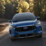 A blue 2023 Ford Escape is shown from the front driving on a winding road.