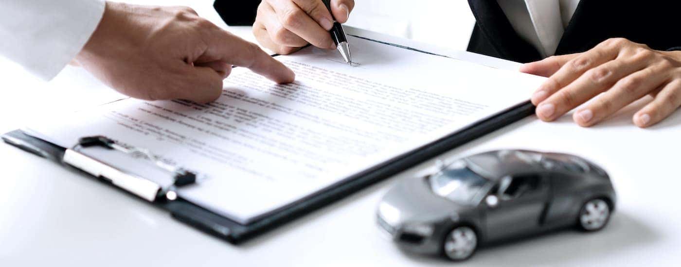 A salesperson is shown pointing at financing paperwork.