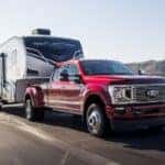 A red 2022 Ford F-350 is shown from the front at an angle while towing a camper.