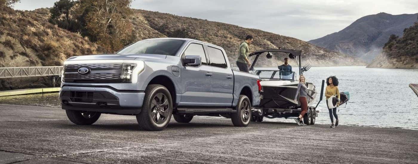 A silver 2024 Ford F-150 Lightning for sale is shown towing a boat.