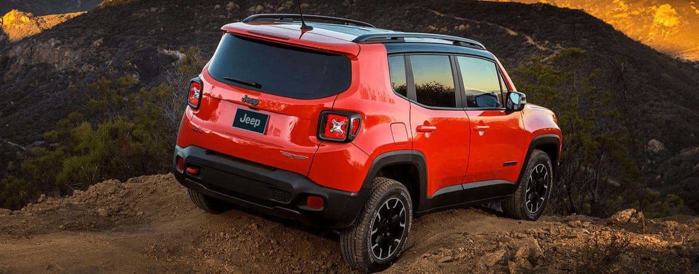 An orange 2023 Jeep Renegade is shown from the rear while off-roading on a rocky trail.