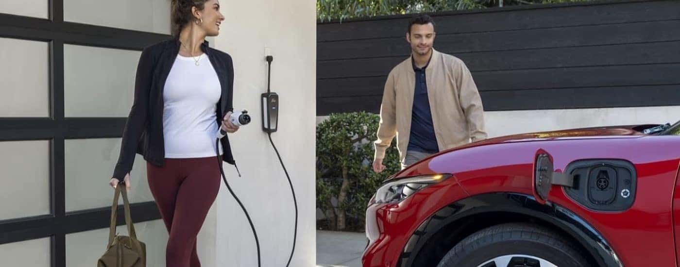 A person is shown holding a charge cable next to a red 2021 Ford Mustang Mach-E.