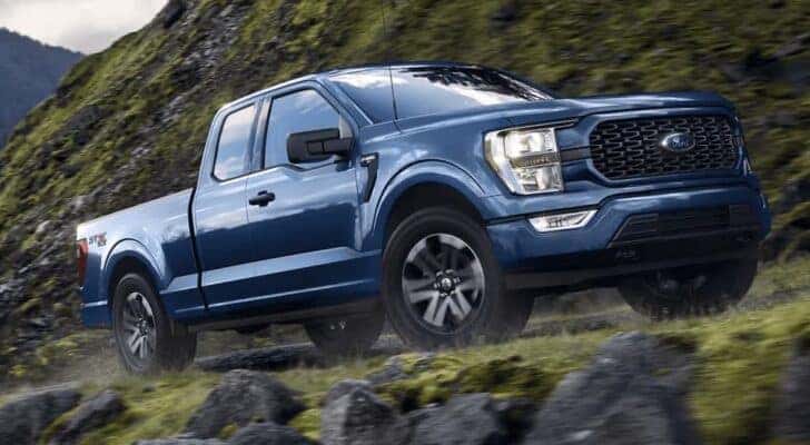 A blue 2023 Ford F-150 STX is shown from the side while off-road after leaving a truck dealership.