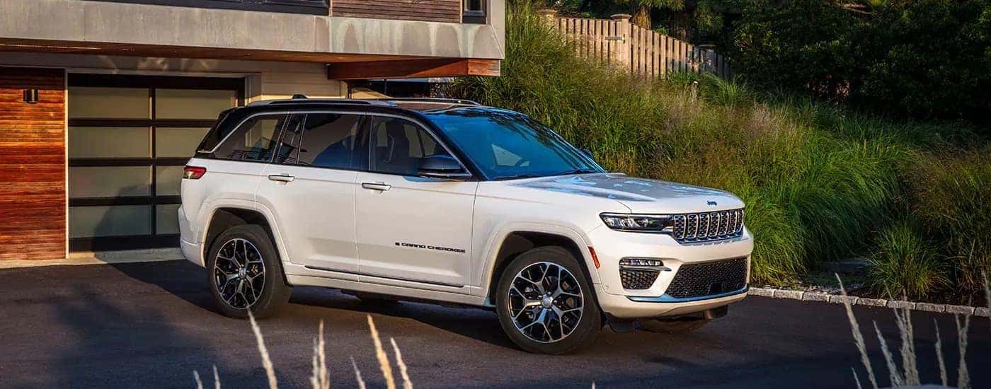 A white 2023 Jeep Grand Cherokee is shown from the side while parked in a driveway.