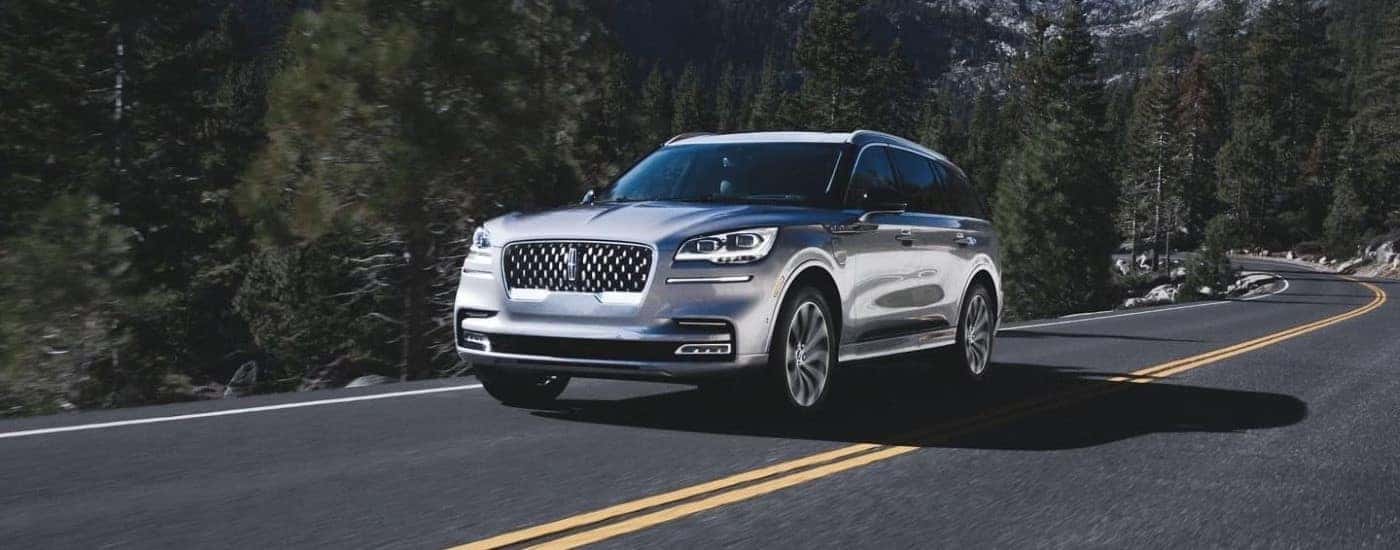 A silver 2023 Lincoln Aviator PHEV is shown driving on a tree lined road after comparing hybrid vs plug-in hybrid vehicles.