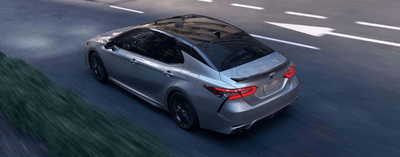 A silver 2023 Toyota Camry Hybrid is shown from a high angle driving on a city street.