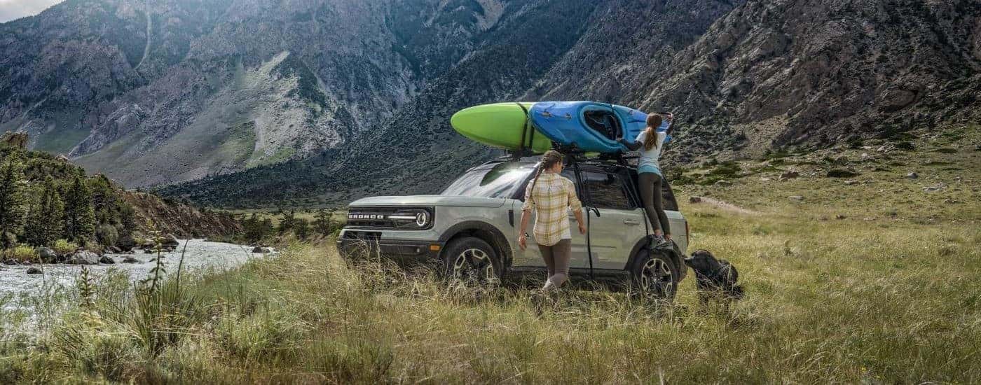 A silver 2021 Ford Bronco Sport is shown next to a river with kayaks on the roof.