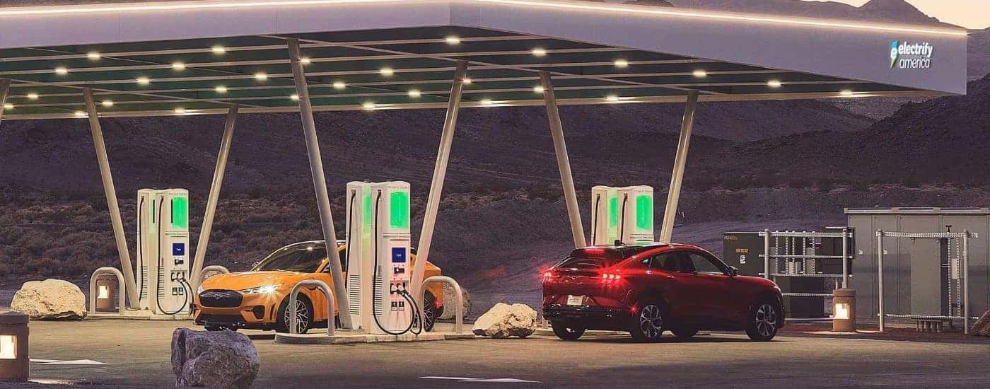 A yellow and a red 2022 Ford Mustang Mach-E are shown at a charging station.