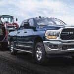 A blue 2024 Ram 2500 Laramie is shown towing a tractor on a trailer.