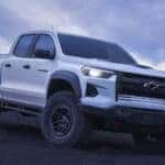 A white 2024 Chevy Colorado is shown driving off-road after visiting a dealer with trucks for sale.
