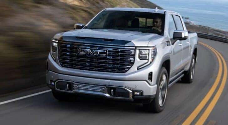 A silver 2024 GMC Sierra 1500 is shown driving on a highway after viewing trucks for sale near Alamosa.