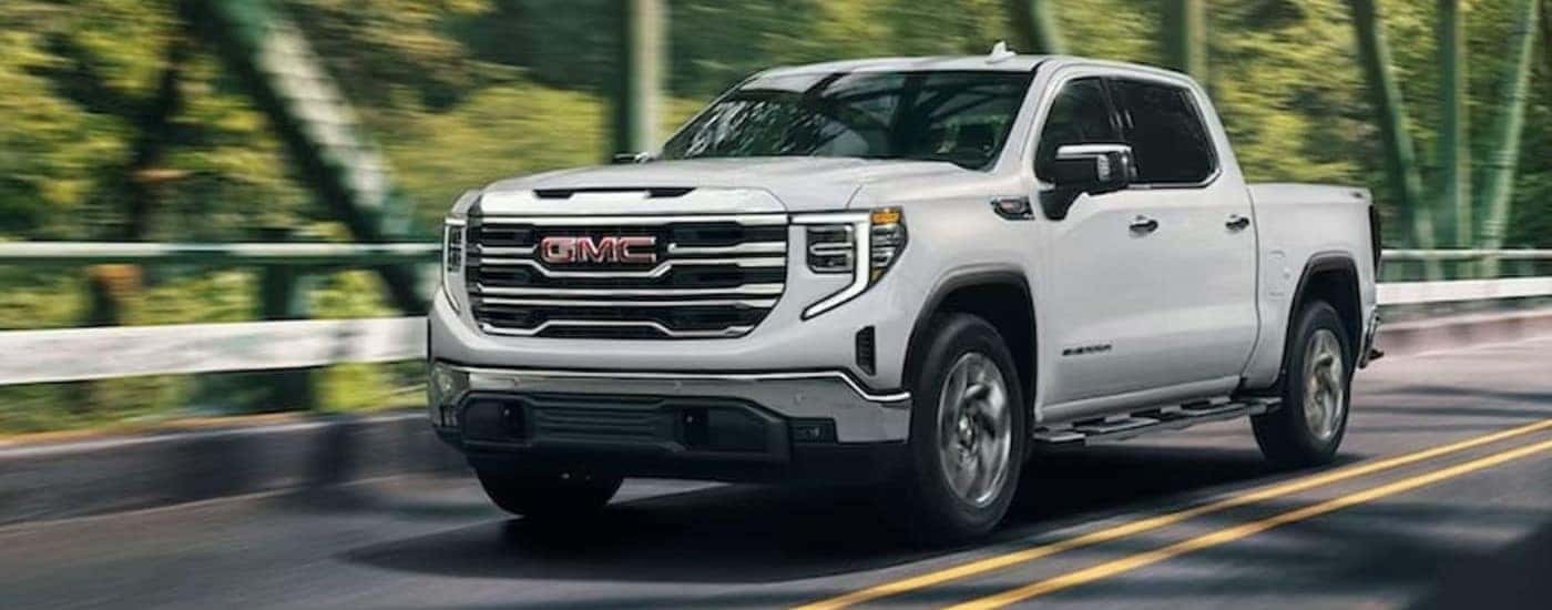 A white 2024 GMC Sierra 1500 SLE is shown driving on a bridge.