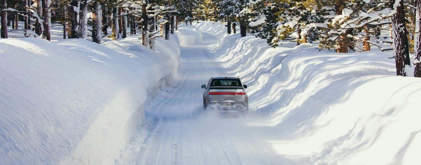 A silver 2024 Rivian R1T is shown driving on a snowy path.