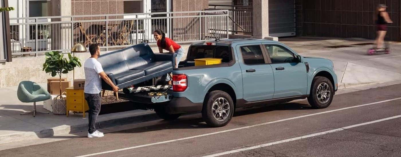 Two people loading a couch into the bed of a blue 2022 Ford Maverick. 