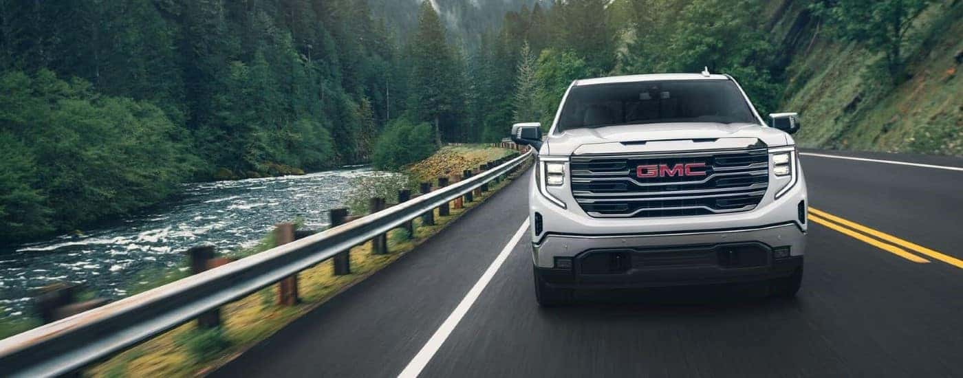 Front view of a white 2024 GMC Sierra 1500 SLE driving down a road.