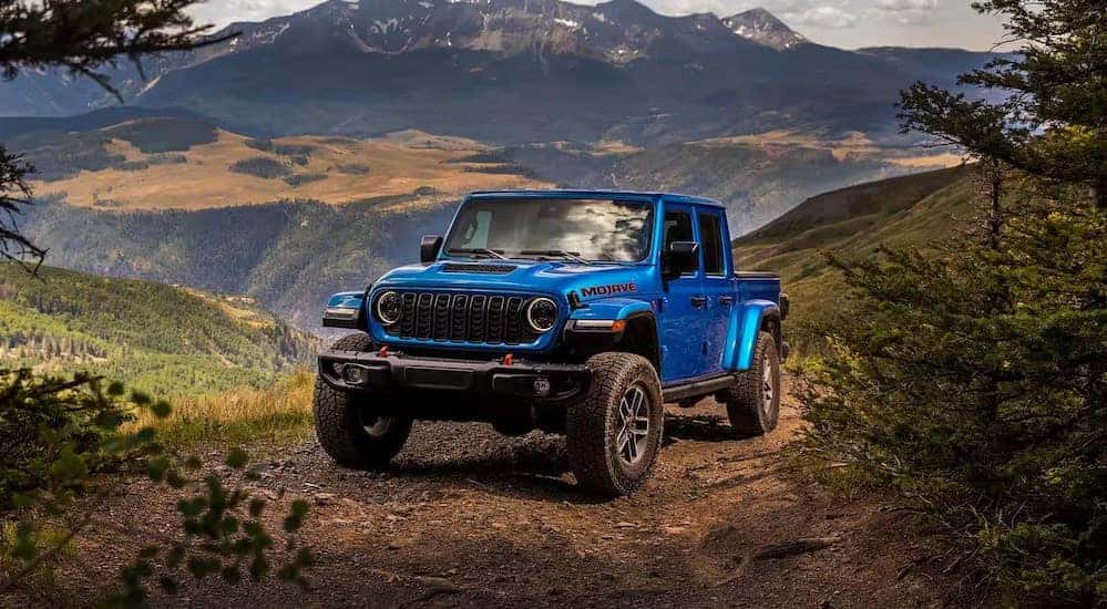 A blue 2025 Jeep Gladiator Mojave is shown parked off-road after visiting a Jeep dealer.
