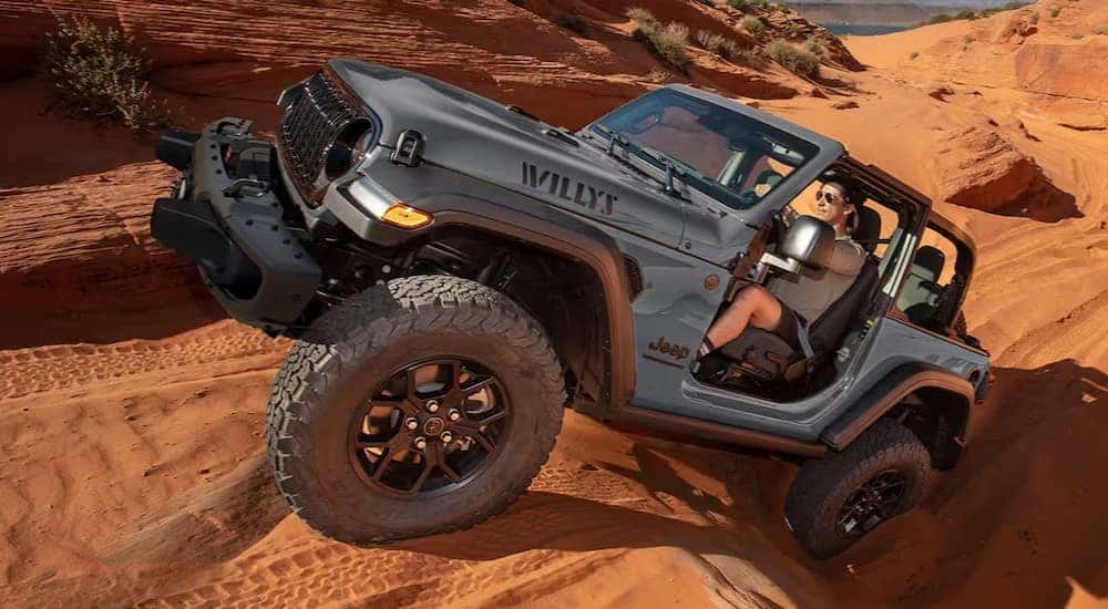 A gray 2025 Jeep Wrangler Willys is shown driving off-road.