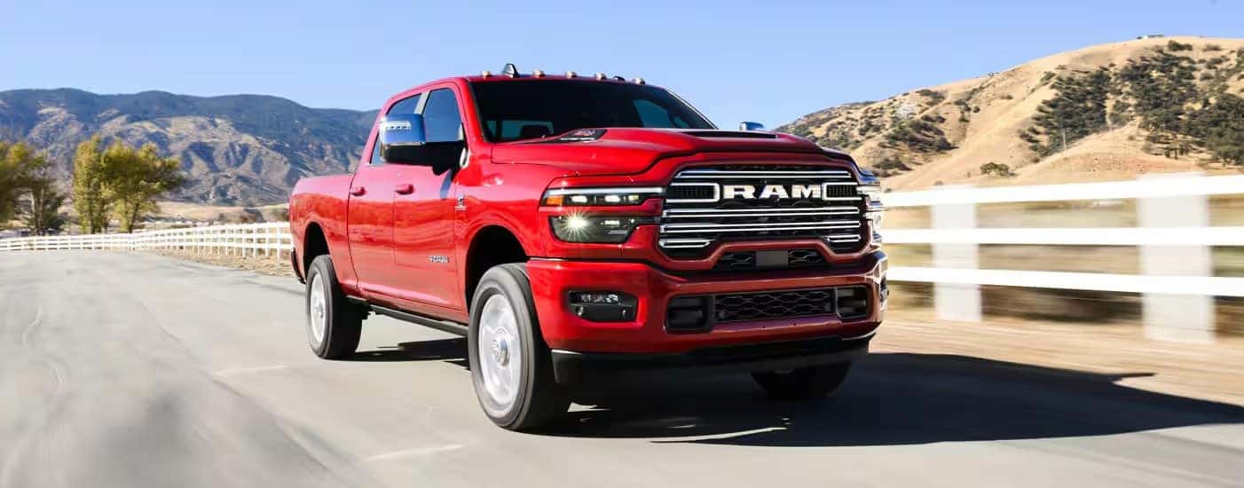 A red 2025 Ram 2500 is shown driving near a white fence.
