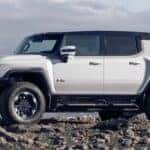 A white 2025 GMC Hummer EV SUV is shown parked off-road.
