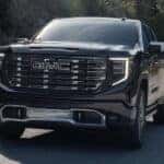 A black 2025 GMC Sierra 1500 Denali Ultimate driving from a GMC dealer.