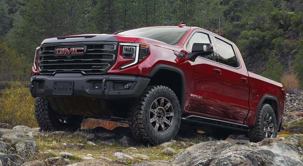 A red 2025 GMC Sierra 1500 AT4X parked off-road near a forest.